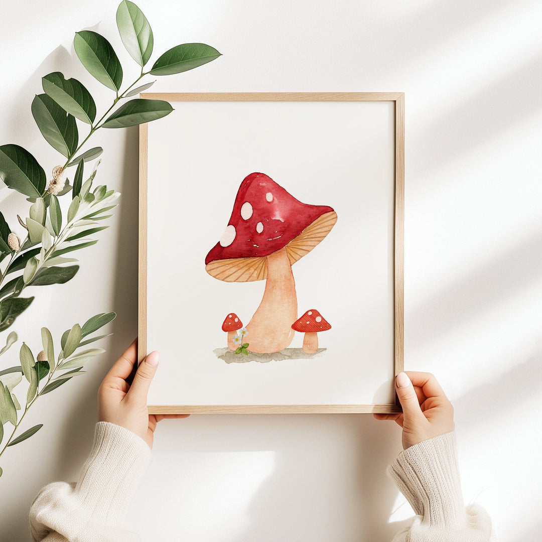 Watercolor illustration of a red and white spotted mushroom with two smaller mushrooms beside it, painted in soft earthy tones on a white background